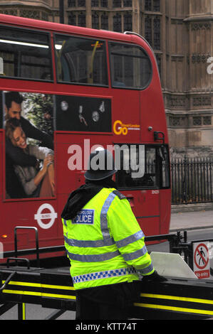 a metropolitan police officer wearing a high visibility vest or jacket on duty at the palace of Westminster or the houses of parliament with a red bus Stock Photo