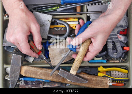 The old grandfather of the house repairman  examines rusty tools in his tool box. Nostalgia for a stormy technical youth concept. Stock Photo