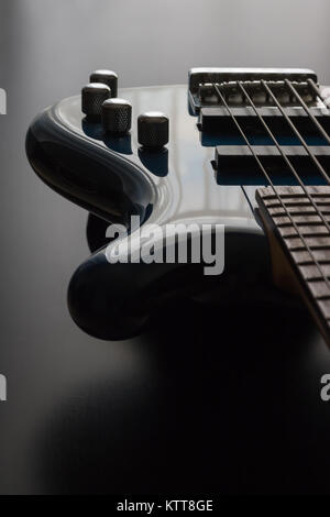 A blue five string bass guitar is strategically positioned in the frame with a black wooden background. This is a darker image which emphasizes the sl Stock Photo