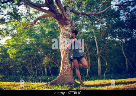 Afro american young girl hiding with dslr photo camera behind the old big tree in the park Stock Photo