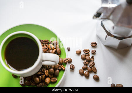 High-angle shot of an Italian Moka pot (coffee maker) and a green Espresso cup with coffee beans on white background Stock Photo