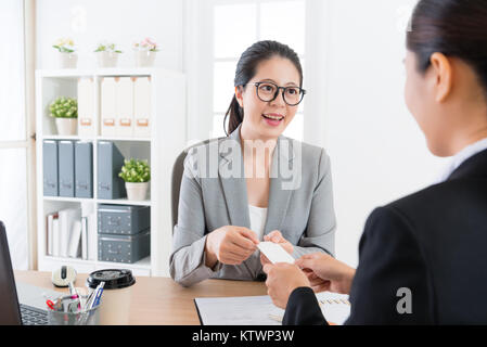 smiling beauty female manager giving young office worker sales girl business card when they discussing company new cooperation scheme. Stock Photo