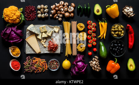 Different fresh ingredients for cooking italian pasta, spaghetti, fettuccine, fusilli and vegetables on a black background. Flat lay, top view. Stock Photo