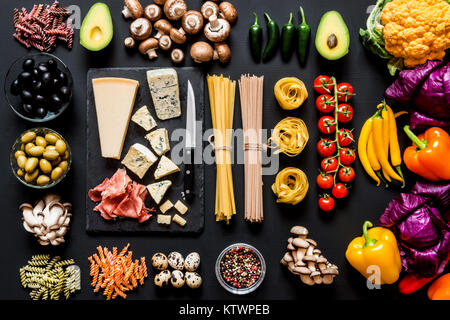 Different fresh ingredients for cooking italian pasta, spaghetti, fettuccine, fusilli and vegetables on a black background. Flat lay, top view. Stock Photo