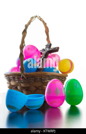 A brown basket is full of decorated easter eggs. A crucifix is among the eggs in the basket.  Standing up in front of the basket are three decorated e Stock Photo