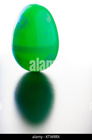 A decorated green Easter egg is standing stranding up on a reflective table top surface. The egg casts a green shadow. The background white Stock Photo