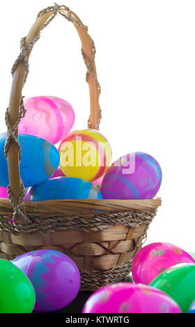 A brown basket is full of decorated easter eggs. Scattered in front of the basket are decorated easter eggs. All the items cast a reflection on the ta Stock Photo