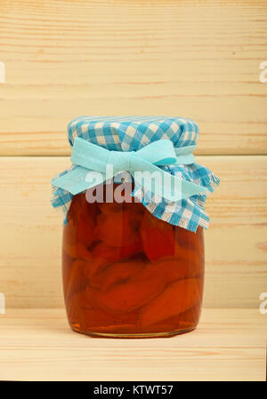 Close up of one glass jar of homemade quince jam with textile top decoration and ribbon bow over white beige painted vintage wooden planks background, Stock Photo