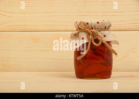 Close up of one glass jar of homemade quince jam with textile top decoration and twine bow over white beige painted vintage wooden planks background,  Stock Photo