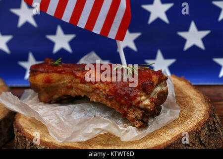 Portion of cooked pork spare ribs in bbq sauce on paper parchment and wood cut under American flag, close up, high angle view Stock Photo