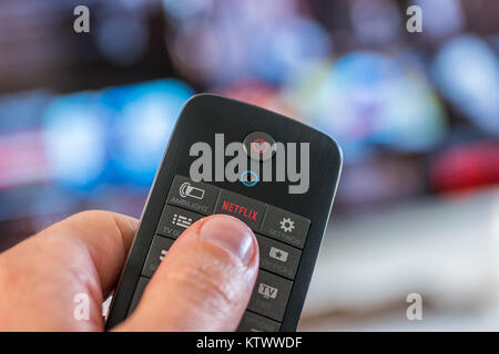 Man holds a remote control and push a Netflix button. Netflix Inc. is an American company founded specializes in and provides streaming media and vid Stock Photo