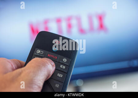 Man holds a remote control and selects a movie from Netflix. Netflix is an entertainment company, specializes in and provides streaming media and vide Stock Photo