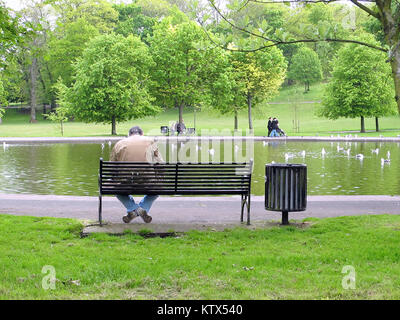 Queen's Park Glasgow,UK single man unemployed sitting on park bench next to pond green trees sunny afternoon depressed lonely hairmless