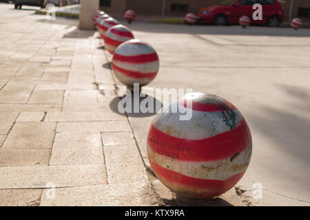 Red and white bollards on stone sidewalk Stock Photo