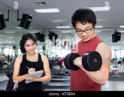 handsome young muscle man working with dumbbell with beautiful young female trainer in gym Stock Photo