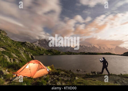 Hiker and tent on the shore of Lacs De Cheserys at night with Mont Blanc massif in background, Chamonix, Haute Savoie, France, French Alps, Europe Stock Photo