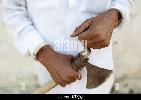 Close-up of hands of old indian man in white outfit holding an axe, in a village near Pushkar, Rajasthan, India. Stock Photo