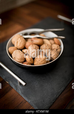 A bowl of mixed whole nuts in their shells including walnuts, hazelnuts, almonds and pecans with a nut cracker Stock Photo