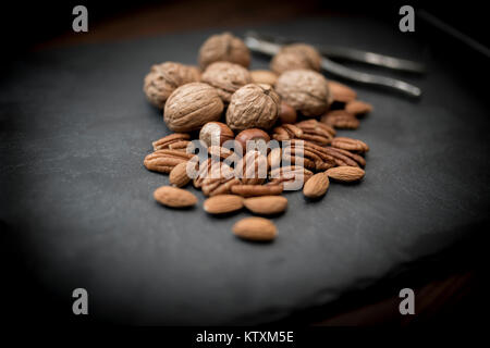 A healthy selection of mixed whole and shelled nuts including walnuts, hazelnuts, almonds and pecans with a nut cracker Stock Photo