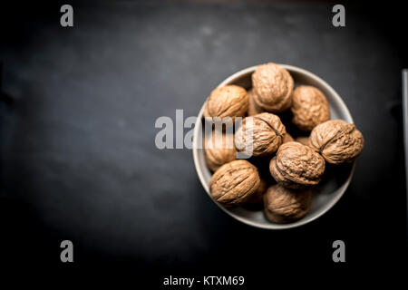A bowl of whole walnuts in their shells in a bowl shot from above on a black slate background Stock Photo