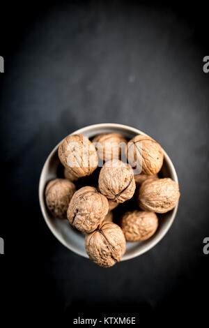 A bowl of whole walnuts in their shells in a bowl shot from above on a natural black slate background Stock Photo