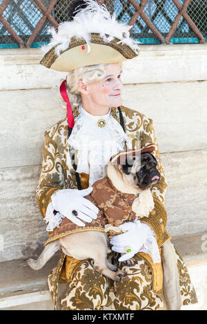 Venice carnival, Veneto, Italy, Man in classic noblemans costume with a pug dog in matching brown seated at the Doges Palace Stock Photo