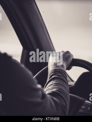 Person with hand on steering wheel driving down the highway, in black and white Stock Photo
