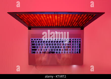 hands typing on a laptop keyboard with red zero and one figures scrolling on screen, top view, red light background Stock Photo