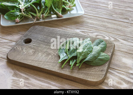 cutting board on a table with spinach leaves, a plate of spinach in the background. Meal preparation concept. Stock Photo