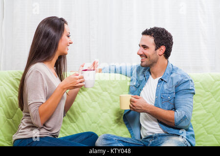 Happy couple sitting on sofa at their home and drinking tea. Stock Photo