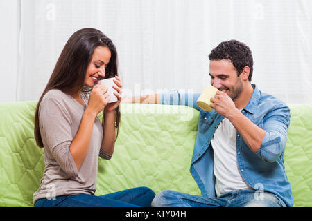 Happy couple sitting on sofa at their home and drinking tea. Stock Photo