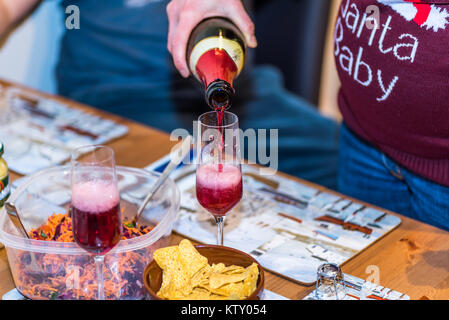 Pregnant female in christmas pullover holding bottle and pouring red non alcoholic wine into champagne glass on table. Stock Photo