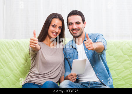 Happy couple sitting on sofa at their home and using digital tablet. Stock Photo