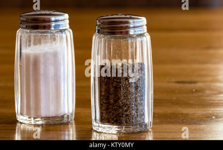 Close up of glass salt and pepper shakers or salt and pepper pots on a wooden table ,very common dining condiments seen on any table at meal times Stock Photo