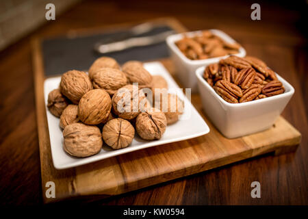 A healthy and nutritious selection of nuts on a wooden serving board with walnuts, pecans, and almonds in contemporary white bowl and plates Stock Photo