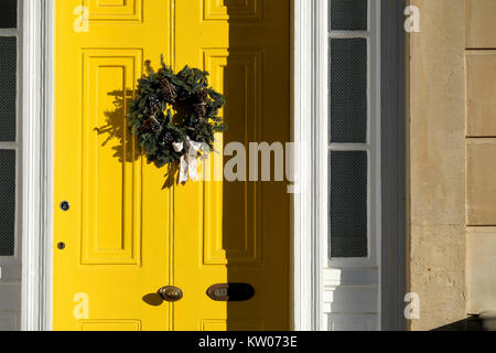 A Christmas wreath fastened to a bright yellw painted house door. Its an old victorian house in Clifton, Bristol on a bright crisp winters day Stock Photo