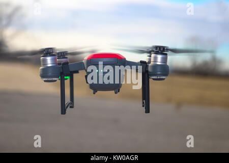Small red and grey drone with landing gear attached and battery at half charge flying against blurred background Stock Photo