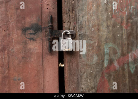 Old wooden door, covered with pink faded oblezshaya paint and closed on a padlock, vintage. Stock Photo