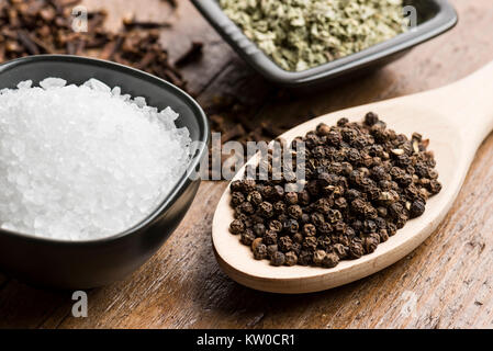 peppercorn in spoon with natural salt and other spices on wooden table. Stock Photo