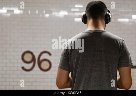 Young African Amercian man with headphones waiting for a subway train at 96th street in New York City, USA. Stock Photo