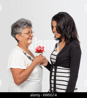 An smiling girl and an smiling old woman holding a red flower with her hand Stock Photo