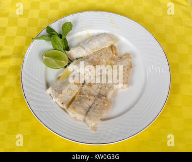 A white filet of fish served in a white dish with a lemon slide Stock Photo