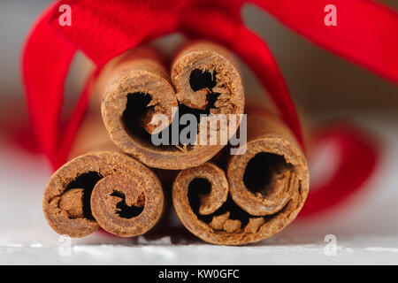 Festive wrapped cinnamon sticks with red ribbon on white textured background. Macro shot, selective focus Stock Photo