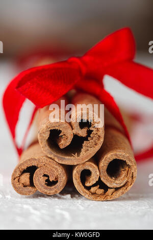 Festive wrapped cinnamon sticks with red ribbon on white textured background. Macro shot, selective focus Stock Photo