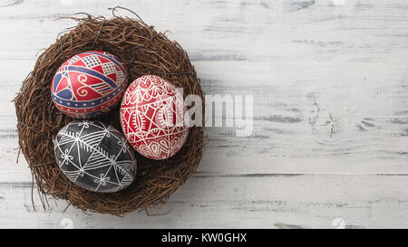 Pysanky in the nest on white wooden background. Easter eggs decorated with wax-resist dyeing technique, traditional for Eastern European countries, wi Stock Photo