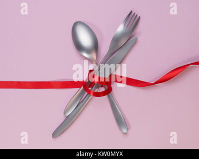 Fork, spoon and knife tied with a red ribbon on pink background. Food, restaurant and table setting theme Stock Photo