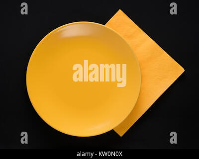 Yellow empty plate and paper napkin on black background. Top view Stock Photo