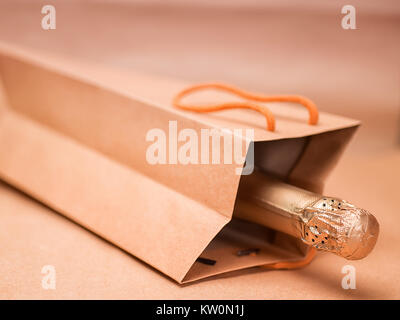 Sparkling wine in craft gift bag on abstract craft paper background. Soft toned image, selective focus Stock Photo