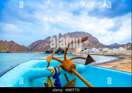 Old, rusty anchor resting on a fishing boat, blue sky and mountains. Stock Photo