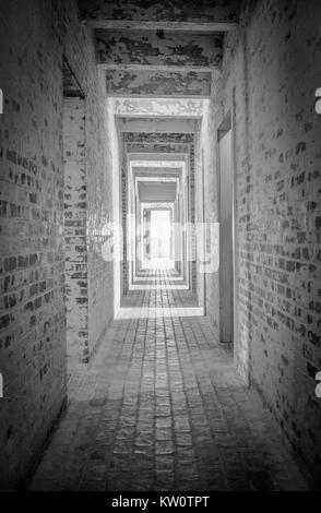 Light At The End Of The Tunnel. Long brick hallway with bright light shining through the open door at the end in vertical orientation. Stock Photo